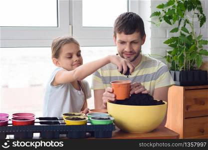 Girl with dad pour earth into pots for planting plants