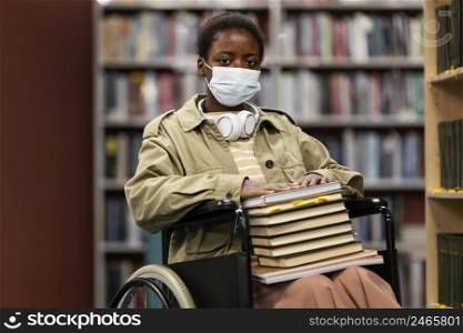 girl with face mask wheelchair holding bunch books