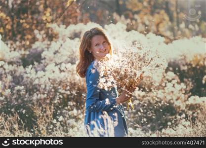 girl with flowers against the setting sun in the autumn afternoon. dandelion fluff in the autumn park.