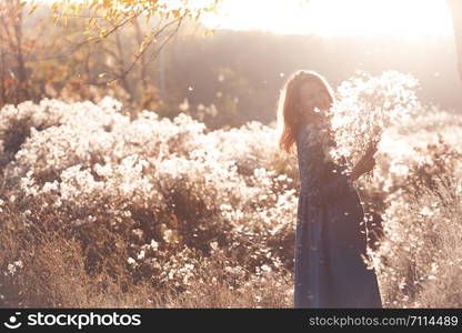 girl with flowers against the setting sun in the autumn afternoon. dandelion fluff in the autumn park.