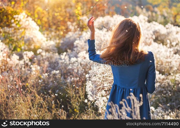 girl with flowers against the setting sun in the autumn afternoon. dandelion fluff in the autumn park.