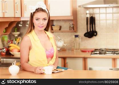 Girl with gingerbread cookies drinking tea coffee.. Pretty pin up girl with heart shape gingerbread cookies drinking tea or coffee at home. Gorgeous young retro woman with hot beverage relaxing in kitchen.