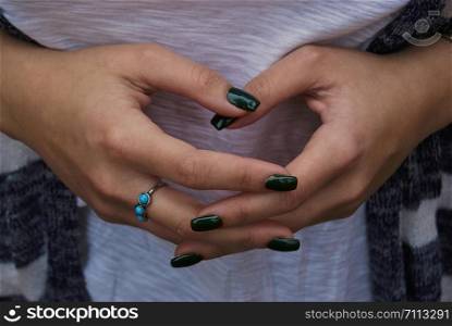 girl with green nails and hands interlaced, with a ring with three turquoise stones