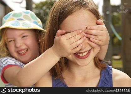 Girl with hands over her sisters eyes in garden