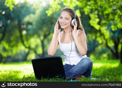 Girl with headphones and a laptop in the park