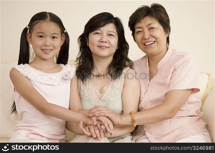 Girl with her mother and grandmother stacking their hands and smiling