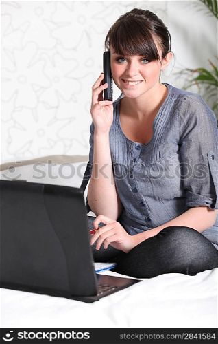 Girl with laptop and phone sitting on her bed