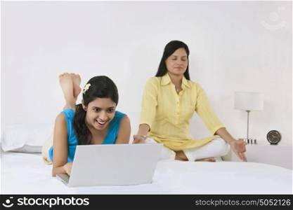 Girl with laptop while mother meditates