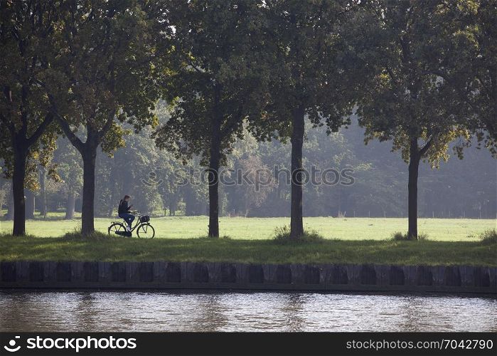 girl with mobile phone on bicycle rides along amsterdam rijn canal in holland between Amsterdam and Utrecht on sunny summer day