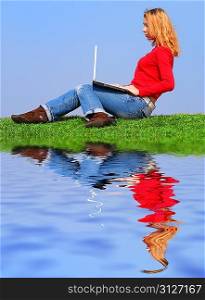 Girl with notebook sitting on grass against sky with reflection on water