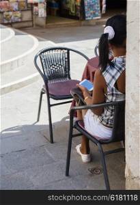 Girl with phone in street cafe, back view
