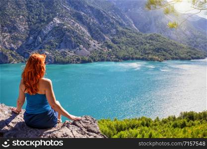 Girl with red hair on cliff top of canyon with green water. Summer landscape. Concept of solitude travel and harmony. Girl with red hair on cliff top of canyon with green water