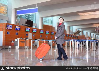 girl with red suitcase standing in airport hall side view