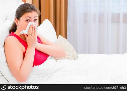 girl with rhinitis blows her nose lying in bed
