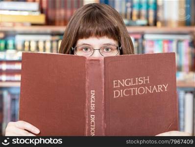 girl with spectacles looks over English Dictionary book in library