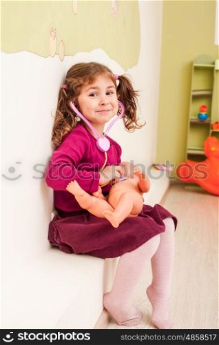 Girl with stethoscope is playing the doctor and listening the doll. Girl plays the doctor