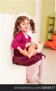 Girl with stethoscope is playing the doctor and listening the doll. Girl plays the doctor