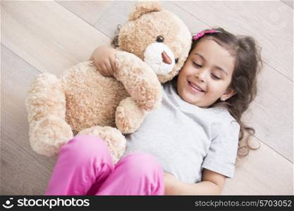 Girl with teddy bear lying on wooden floor at home