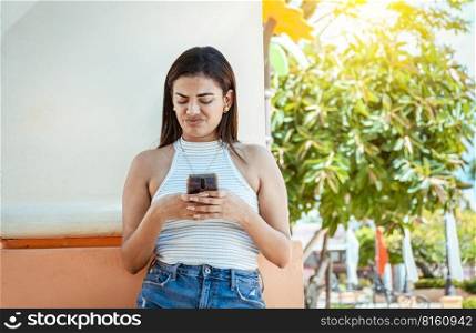 Girl with the cell phone receiving an unpleasant message. Young woman with cell phone reading a message with an unpleasant face. Upset girl frowning reading unpleasant message