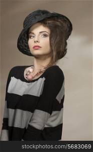 girl with trendy look posing in fashion portrait with elegant black hat, striped dress and pink necklace