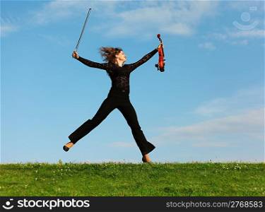 girl with violin jumps on grass against sky