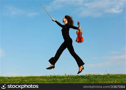 girl with violin jumps on grass against sky