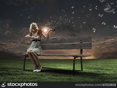 Girl with violin. Young woman sitting on bench and playing violin