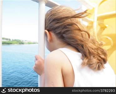 Girl with wind in long blond hair holding onto white railing
