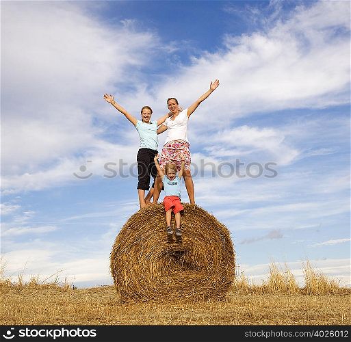 girl, woman, boy standing on hay bale