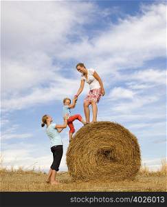 girl, woman help boy to climb hay bale