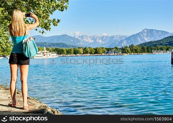 Girl woman shoot photos of mountains at lake Worthersee Klagenfurt. Girl at Worthersee in Klagenfurt shoot photos