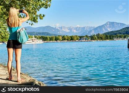 Girl woman shoot photos of mountains at lake Worthersee Klagenfurt. Girl at Worthersee in Klagenfurt shoot photos