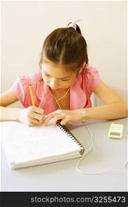 Girl writing on a spiral notebook and listening to an MP3 player
