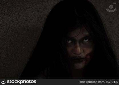 Girl zombie in blood. Asian Woman ghost with blood. Horror creepy scary fear she sitting in a dark house. Hair covering the face, Halloween festival concept