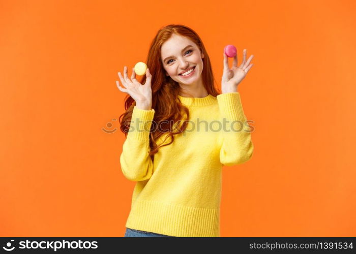 Girlfriend want share dessert, holding two macarons and smiling, suggest bite with lovely grin, tilt head flirty, standing happy orange background, enjoy winter holidays and sweet gifts.. Girlfriend want share dessert, holding two macarons and smiling, suggest bite with lovely grin, tilt head flirty, standing happy orange background, enjoy winter holidays and sweet gifts