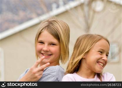 Girls (8-11) gesturing with house in background, smiling, portrait