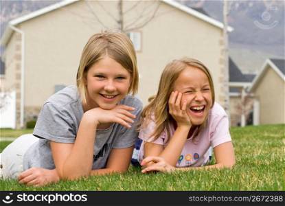Girls (8-11) lying on grass with house in background, portrait