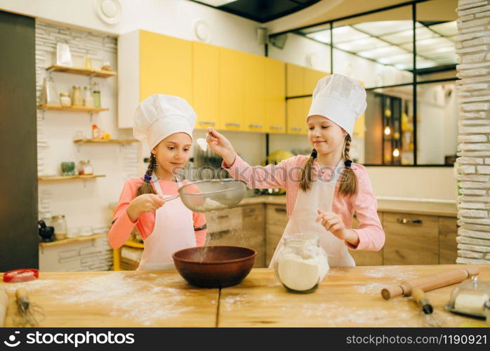 Girls cooks in caps, cookies preparation on the kitchen. Kids cooking pastry, little chefs makes dough, child preparing cake. Girls cooks, cookies preparation on the kitchen