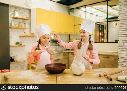 Girls cooks in caps, cookies preparation on the kitchen. Kids cooking pastry, little chefs makes dough, child preparing cake. Girls cooks, cookies preparation on the kitchen