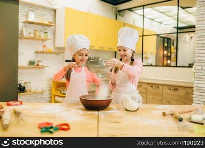Girls cooks in caps, cookies preparation on the kitchen. Kids cooking pastry, little chefs makes dough, child preparing cake