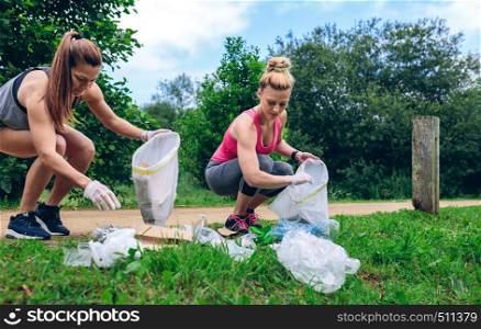Girls crouching with garbage bag picking up trash doing plogging. Girls with garbage bag doing plogging