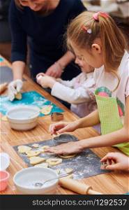 Girls cutting the dough to heart shapes for the cookies. Kids taking part in baking workshop. Baking classes for children, aspiring little chefs. Girls learning to cook. Combining and stirring prepared ingredients. Real people, authentic situations