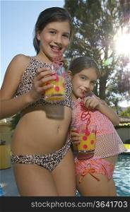 Girls drinking juice from crazy straws on edge of swimming pool, portrait