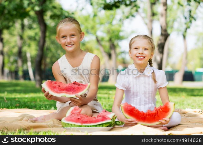 Girls eating watermelon. Cute girls in park eating juicy watermelon