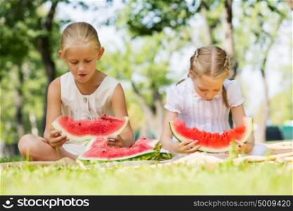 Girls eating watermelon. Cute girls in park eating juicy watermelon