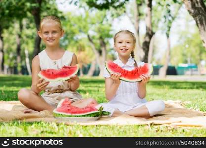 Girls eating watermelon. Cute girls in park eating juicy watermelon
