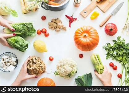 Girls hands holding various seasonal vegetables on white background with pumpkins, pot, cutting board and knife, top view. Flat lay. Cooking party. Healthy lifestyle and eating. Low carb food
