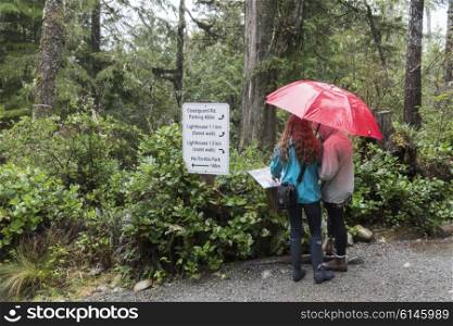 Girls holding an umbrella looking at sign board, Pacific Rim National Park Reserve, Ucluelet, Vancouver Island, British Columbia, Canada