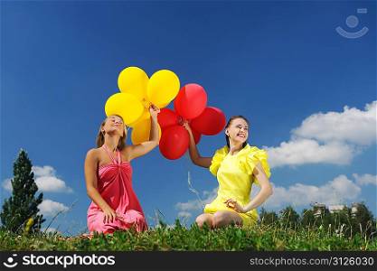 Girls holding balloons against sky