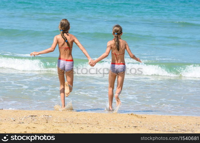 Girls holding hands run into the sea